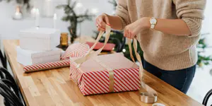 Geschenk mit rot-weißem Papier und goldener Schleife wird verpackt