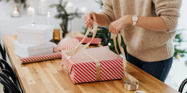 Geschenk mit rot-weißem Papier und goldener Schleife wird verpackt