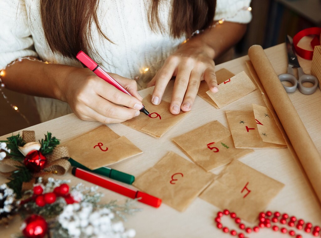 Adventskalender selber basteln – 10 kreative ideen für kinder, eltern und familien 2 Zwei hände von oben, die einen adventskalender mit roten zahlen beschriften