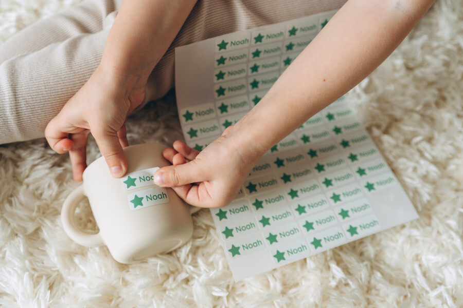 Kreative montessori‑bastelideen: so fördern kleine hände die fantasie 4 Kinderhände kleben einen personalisierten namensaufkleber mit dem text "noah" auf eine tasse