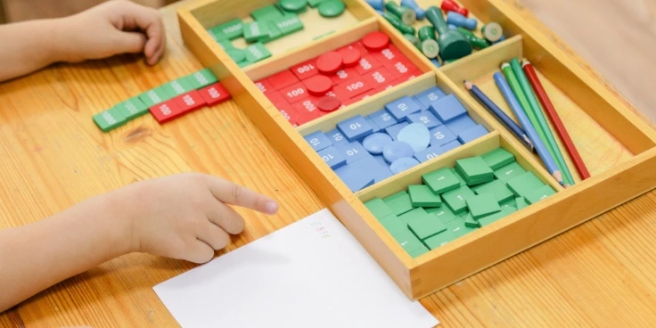 Kind arbeitet mit montessori-mathematikmaterialien auf einem holztisch.