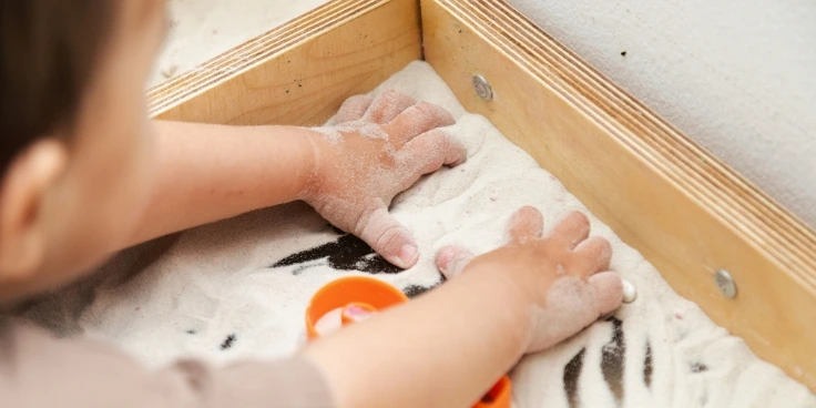 Kind schreibt zahlen in einer montessori-sandwanne.
