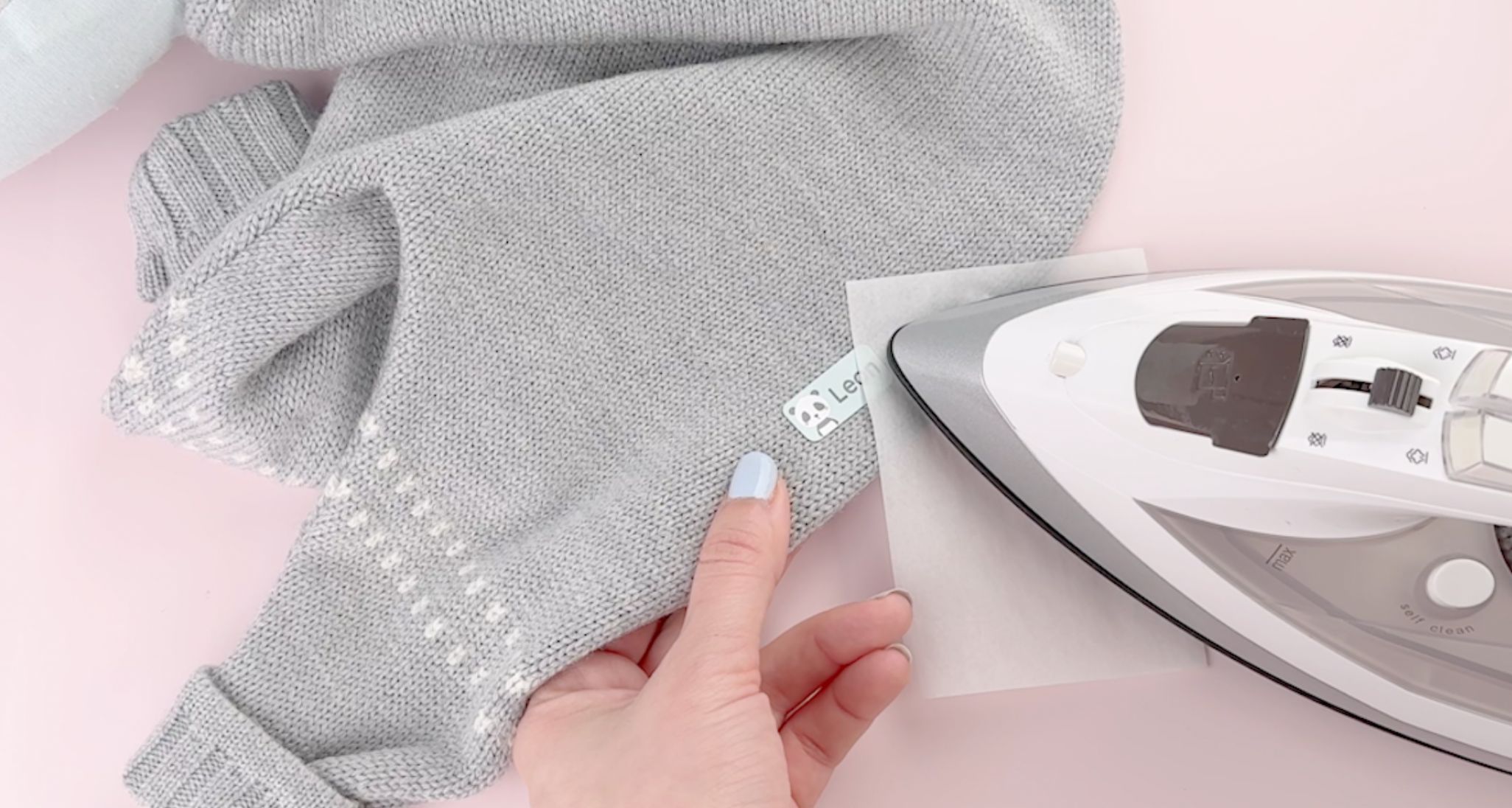Bügeletikett mit dem namen leon wird auf ein graues gestricktes babykleidungsstück aufgebügelt