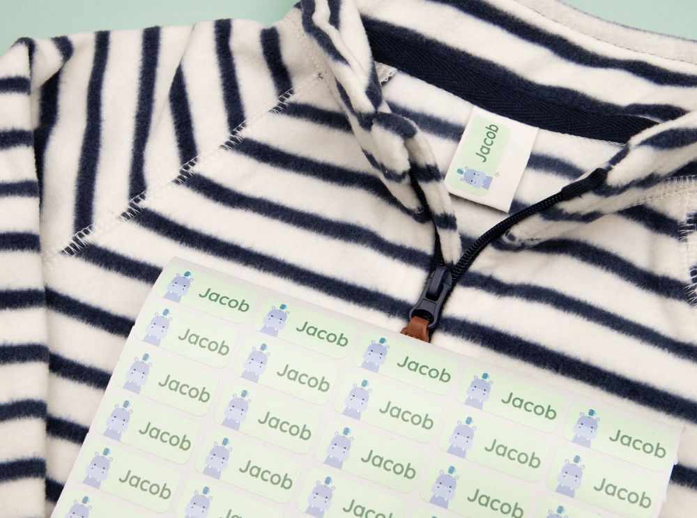 Bogen mit grünen Namensaufklebern mit Nilpferdmotiv, ein Aufkleber platziert auf einem gestreiften Kinder-Shirt