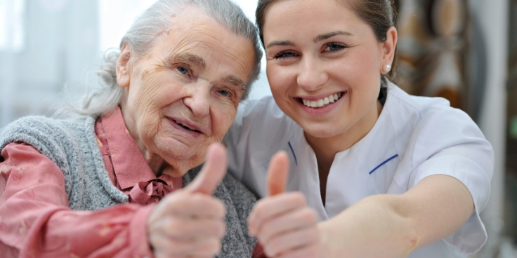 Seniorin und pflegekraft zeigen gemeinsam daumen hoch, als zeichen für zufriedenheit und gute organisation mit bügeletiketten im pflegeheim.