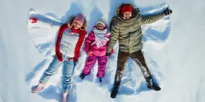 Familie macht Schneeengel im Freien und trägt warme Winterkleidung.