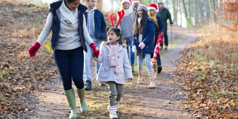 Familie unternimmt einen winterlichen spaziergang im wald, kinder tragen weihnachtliche accessoires.