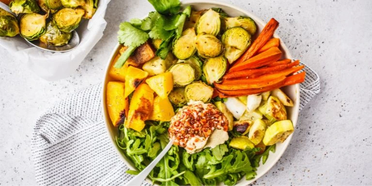 Ein buntes, gesundes wintergericht mit geröstetem gemüse, rosenkohl, kürbis, hummus und frischen kräutern