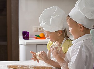 Kinder mit weißen Kochmützen kneten gemeinsam Pizzateig in der Küche
