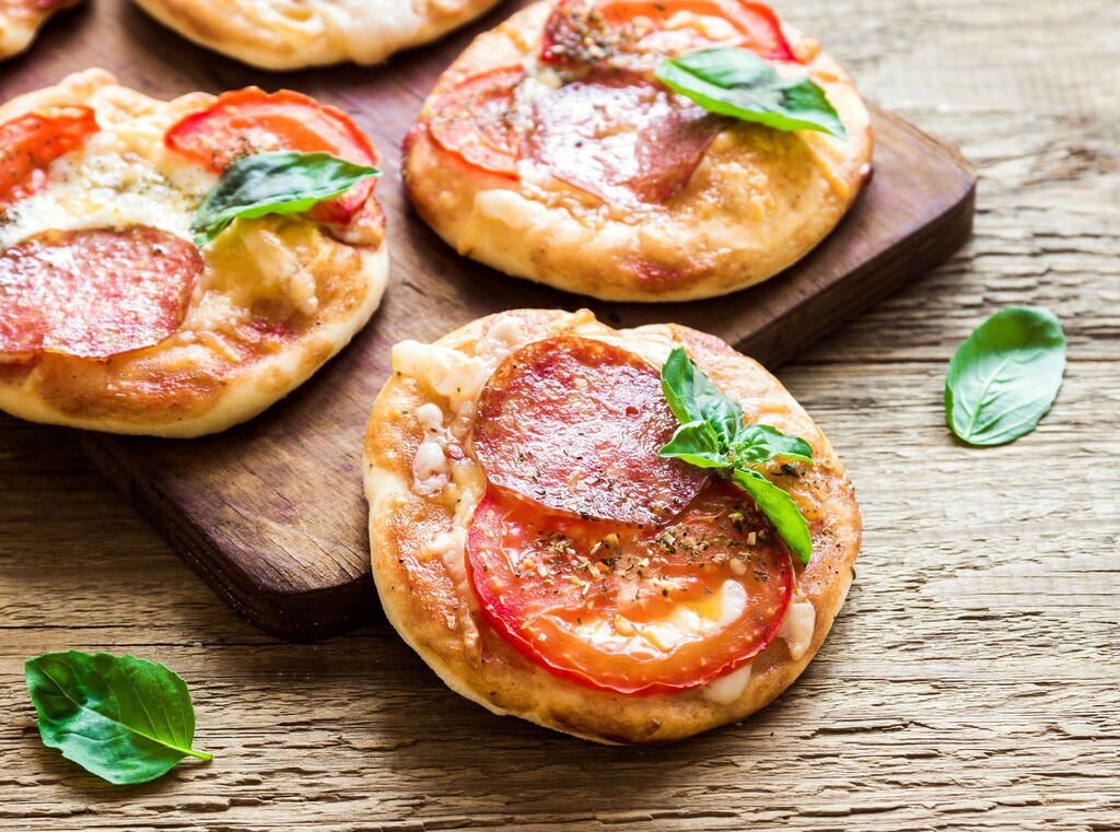Frisch gebackene mini-pizzen mit salami, tomaten und basilikum