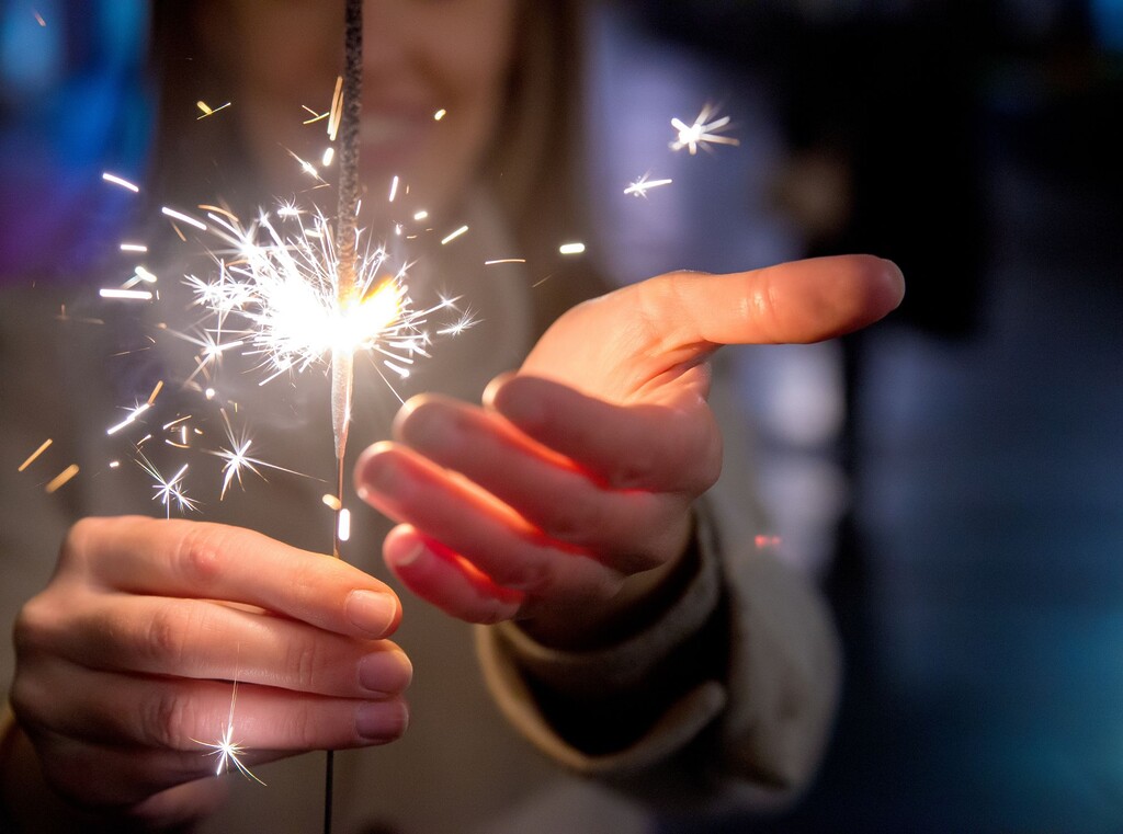 Silvester mit kindern: ideen für ein unvergessliches fest 1 Hand hält brennende wunderkerze mit funkenflug, perfekt für silvesterstimmung