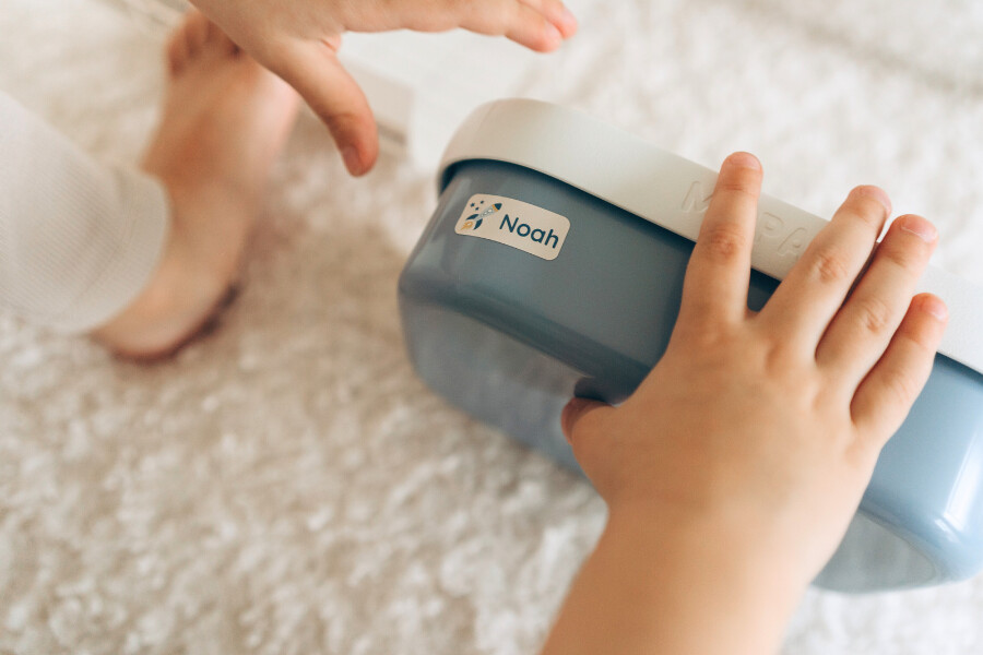 Nie wieder verloren: namensaufkleber für kita und schule 4 Kinderhand mit blauer brotdose und personalisiertem sticker mit 'noah' und raketenmotiv.