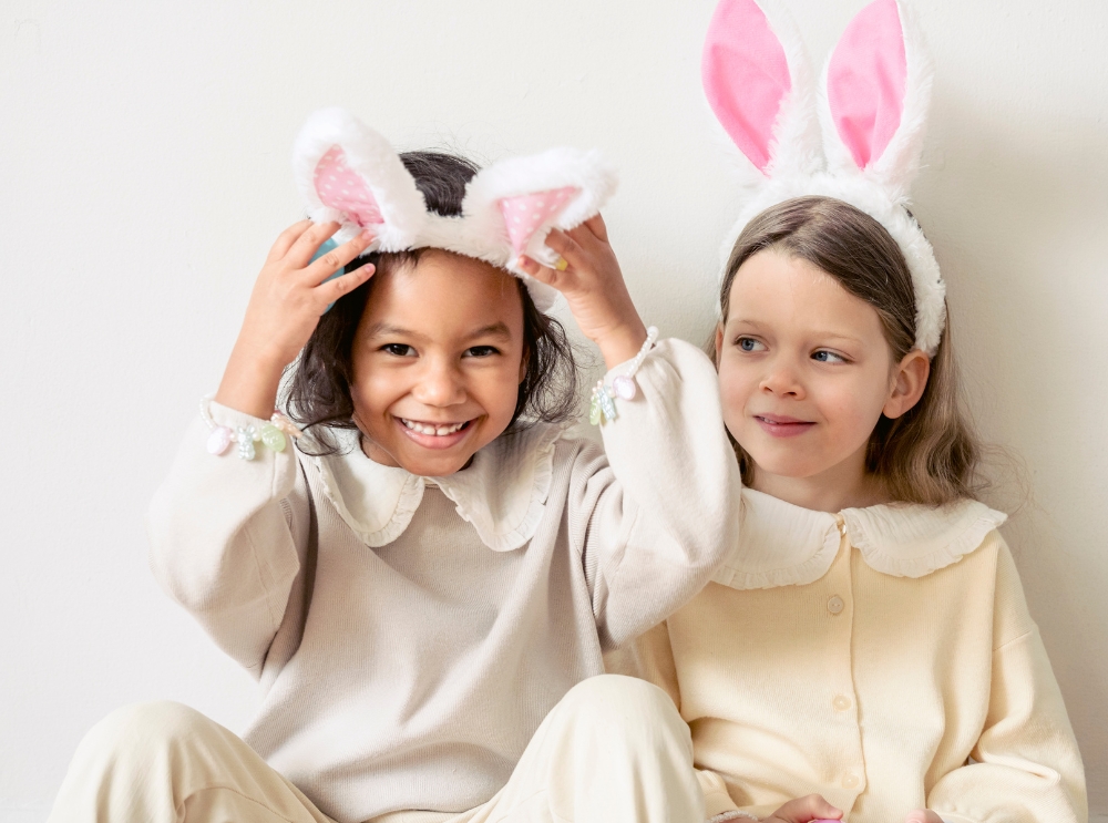 Zwei Vorschulkinder mit Hasenohren-Stirnband, lächelnd und zusammen sitzend