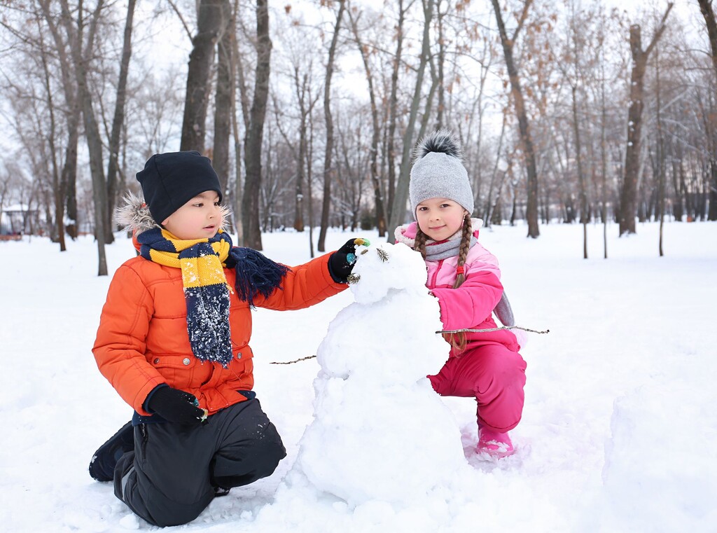 Two children playing in the snow and building a snowman together in a winter park.