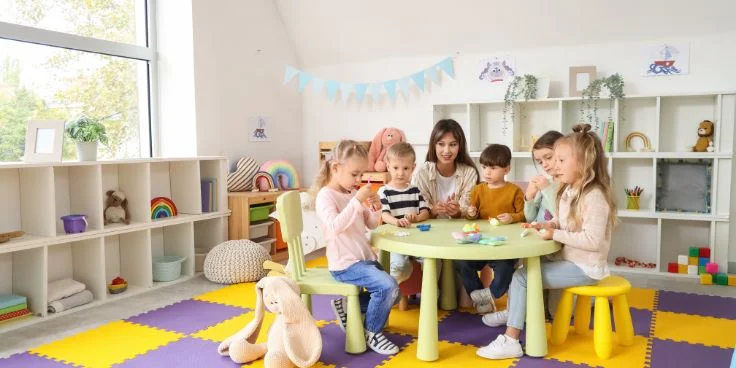 Erzieherin mit Kindern am Spieltisch im Kindergarten